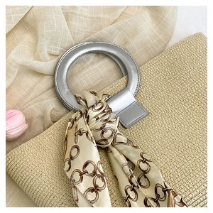 Close-up of beige woven tote bag featuring silver metal handles and decorative silk scarf