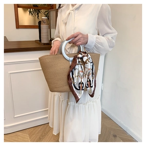Detail of woven straw tote bag with silver metal handles and decorative silk scarf