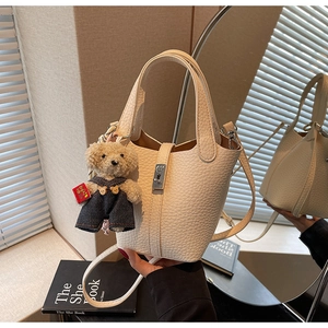 Close-up of cream bucket bag in pebble leather with a cute bear plush charm and strap