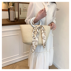 Detail view of woven straw tote bag with silver metal handle and stylish silk scarf