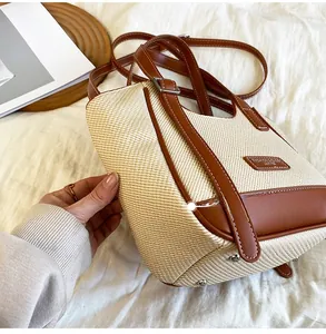 Vue détaillée du sac en paille beige avec garniture en cuir brun et pieds en métal