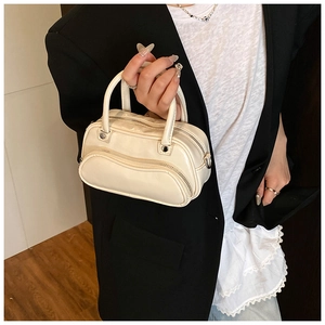 Detail of cream mini handbag with curved zipper and smooth leather texture held by model