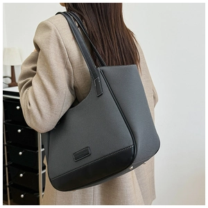 Detalle de bolso tote en lona gris oscuro con ribetes de cuero negro y costuras blancas