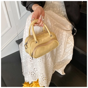 Detail of a yellow patent leather handbag with silver zippers and a double handle design