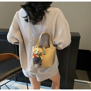 Detail view of beige lychee texture bucket bag with bear charm and floral silk scarf