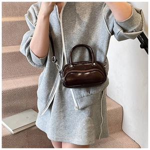 Fashionable dark brown bowling bag with glossy finish worn as a crossbody by a model