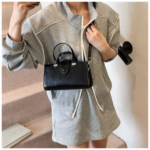 Sac à bandoulière noir brillant minimaliste avec détails argentés sur un escalier moderne