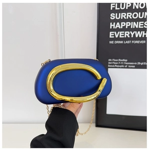 Close-up of a royal blue evening clutch with a large gold C-buckle and thin chain strap