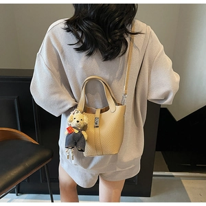 Detailed close-up of a beige pebble leather bucket bag with silver lock and bear charm