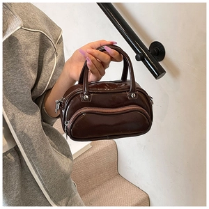Detail of glossy brown faux leather handbag with zipper and top handles in a hand-held shot