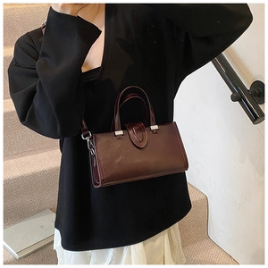 Détail d'un sac bandoulière bordeaux avec boucles argentées et coutures en forme de U