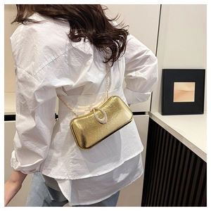 Detail of gold evening clutch with silk texture, rhinestone clasp and chain strap on shoulder