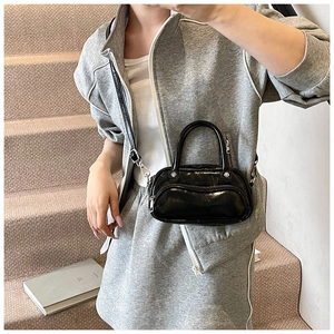 Detail of a shiny black mini crossbody bag with a curved zipper and adjustable strap