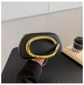 Detail of black matte evening bag with bold gold metal handle and chain strap
