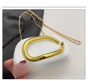 Detail of white pebble leather bag with large gold C-shaped handle and fine chain