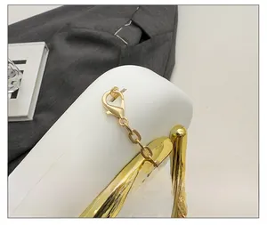 Detailed close-up of premium gold metal lobster clasp and chain on a white leather bag