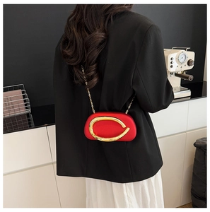 Detail of red lacquered shell bag with gold metal ring and chain strap on shoulder