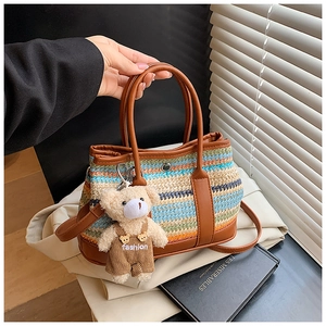 Détail d'un sac en paille tissée à rayures avec bandoulière en cuir et breloque ourson