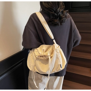 Detailed back view of a beige canvas crossbody bag with drawstring closure on model