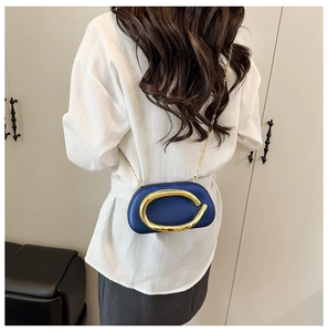 Detail of navy blue oval hard shell crossbody bag with a large gold ring handle and chain