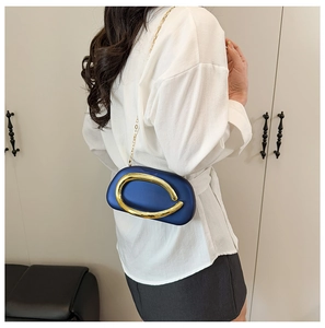 Detail of navy blue hard shell crossbody bag with golden hardware on a model
