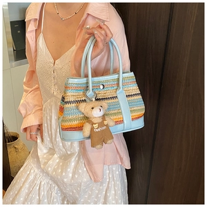 Détail d'un sac à main tissé coloré avec anses bleu clair et pendentif ours en peluche