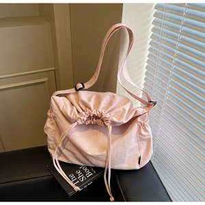 Close-up of pink drawstring canvas shoulder bag with adjustable buckle on leather sofa