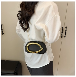 Detail view of black leather shoulder bag with large gold metal ring buckle on white shirt