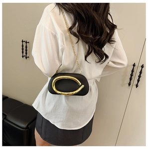 Minimalist black leather square bag featuring a large gold C-buckle and elegant chain strap