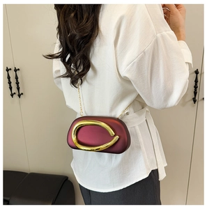 Detail of burgundy matte crossbody bag with gold oval buckle on a white shirt model