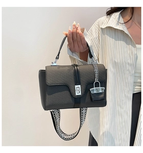 Détail du sac à main noir avec rabat tissé, fermoir argenté et large bandoulière brodée