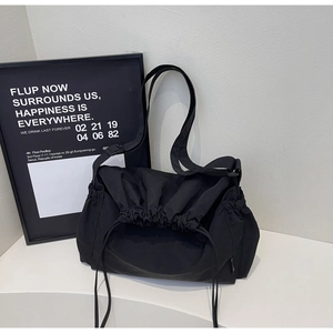 Detail of a large black nylon tote bag featuring a drawstring closure and adjustable strap