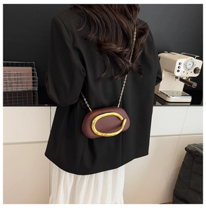Detail view of burgundy mini chain bag with gold buckle on a modern cafe table
