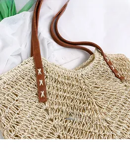 Detail of brown leather handle with white cross-stitch on hollow straw tote bag