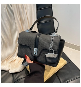 Détail d'un sac noir avec rabat tressé, fermoir argenté et bandoulière large à motifs
