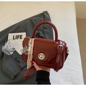 Detail of burgundy crossbody bag with silver lock, metal charm and silk scarf handle
