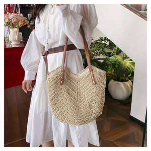 Minimalist straw tote bag with brown leather straps shown on a model in a natural setting