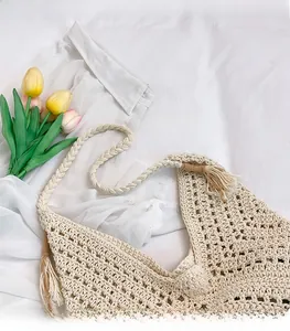 Close-up of beige woven shoulder bag featuring hollow crochet pattern and tassel details