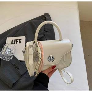 Minimalist beige crossbody handbag with circular metal lock and woven charm on a suit background