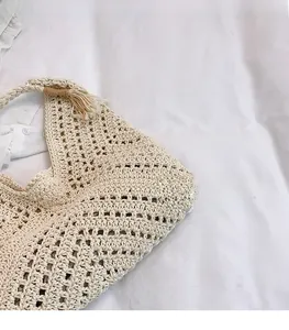 Close-up of beige woven shoulder bag featuring intricate hollow textures and tassel charm