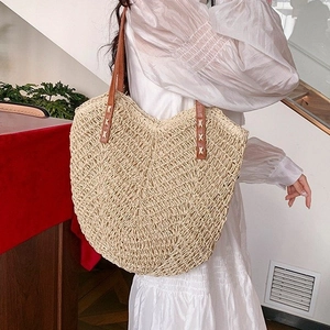 Close-up of minimalist straw tote bag with brown leather straps worn with white dress