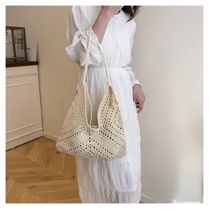 Detail of beige hand-woven crochet tote bag with hollow patterns and tassel charm