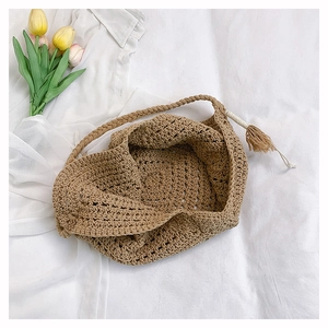 Detail of hand-woven straw shoulder bag with tassel charm on minimalist fabric background