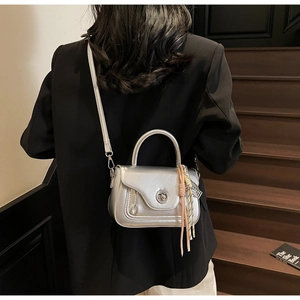 Silver metallic mini handbag with tassel charm and chain strap on modern stairs