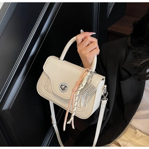 Close-up of cream leather crossbody bag with silk scarf handle and metal abacus charm