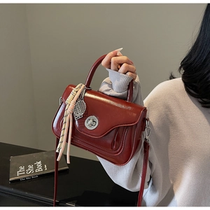 Detail of red-brown glossy leather handbag with silver twist lock and tassel decoration