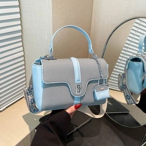 Sac à main en cuir bleu et tissu tissé avec bandoulière brodée sur un bureau en bois