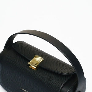 Detail of black woven texture handbag with golden metallic clasp and smooth handle strap