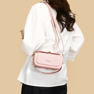 Pink crossbody bag with herringbone weave flap and golden metal hardware shown on model