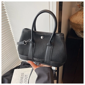 Detail of black pleated bucket bag featuring metallic buckle and rolled top handles